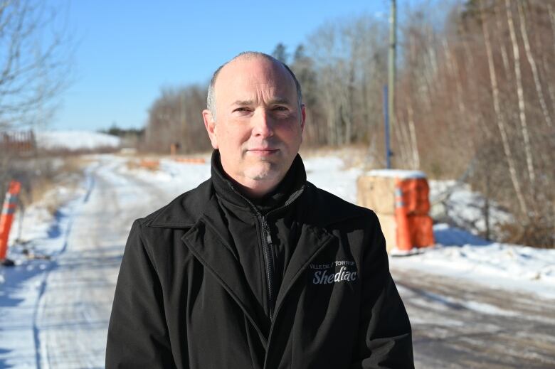 A man in a black jacket with a snowy road in the background.