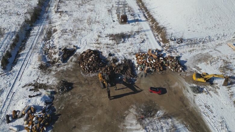 Piles of scrap material with two excavators and a snow-covered rail line. 