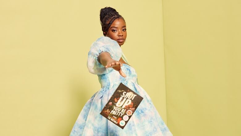 A Black woman wearing a blue and white poofy dress drops a book and looks at the camera. 