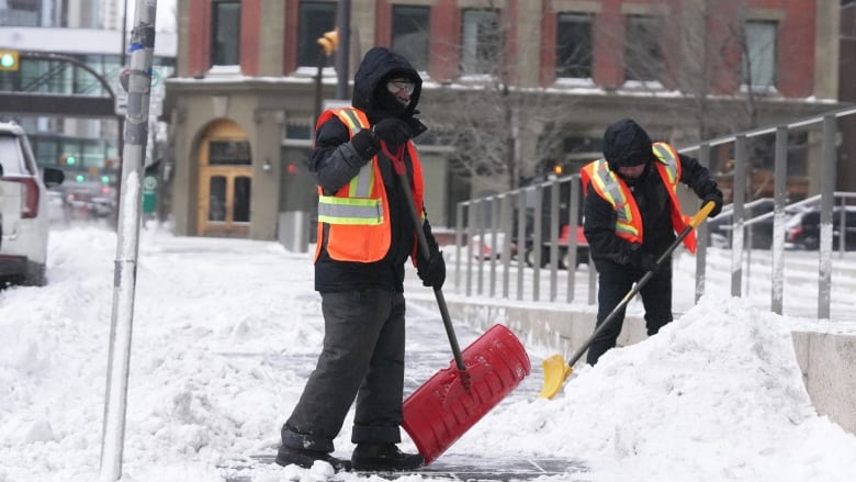 Two people shovel snow.