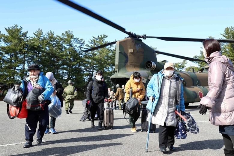 People wearing masks and carrying knapsacks and bags walk from a helicopter.