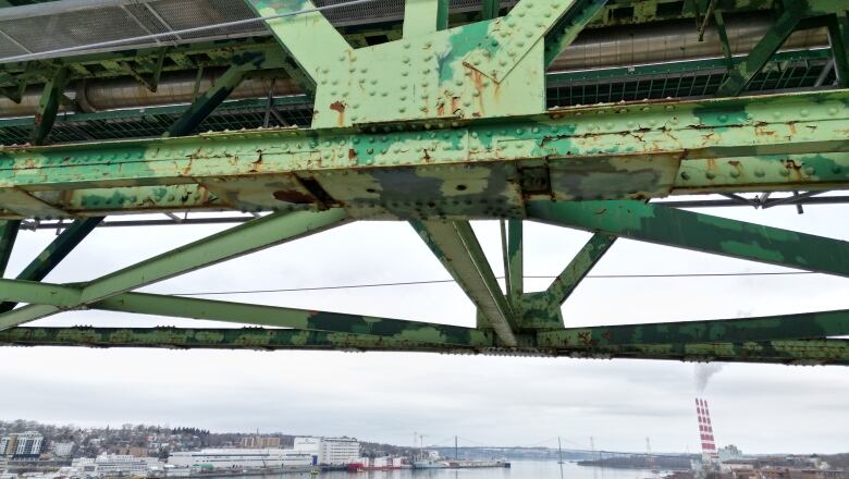 Multiple steel beams in different shades of patchy green are seen on the steelwork, with the harbour and edge of Dartmouth underneath