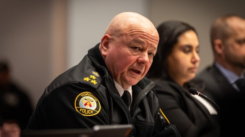 Toronto's police chief, wearing a back jacket with police logo on it, speaks while seated at a city committee table.