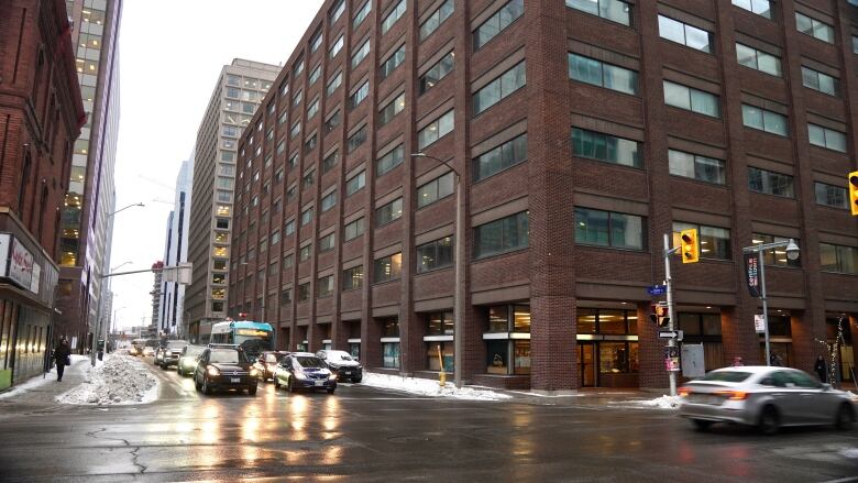 A downtown intersection on a winter day, with several cars waiting for the light to change next to a large brown brick building.