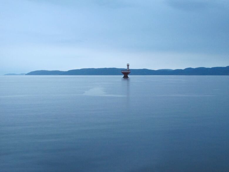 A red and white lighthouse is seen atop a man made structure in a deep estuary