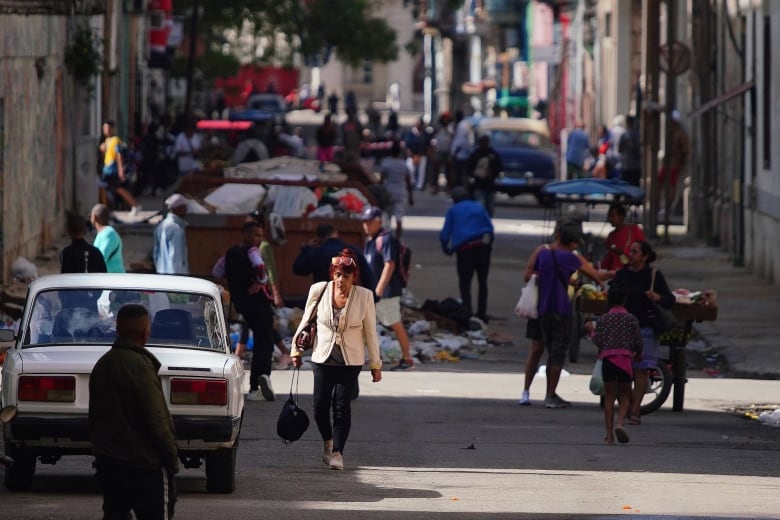 A woman walks down a street with overflowing garbage bins and food carts in the background