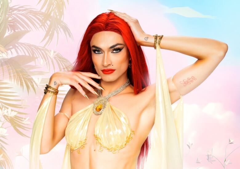 A drag queen in a red wig strikes a pose while wearing a gold bikini top with jewels.