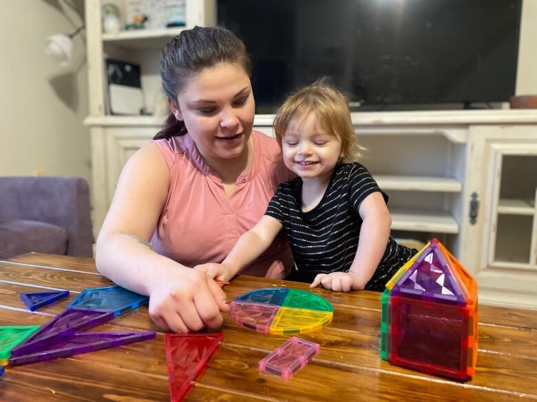 A woman kneels in front of a table with a small girl and they play with table top activities. 