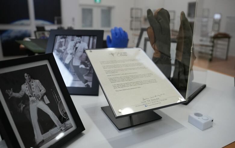 Gloves inside a glass box, with pictures of Elvis Presley next to it.