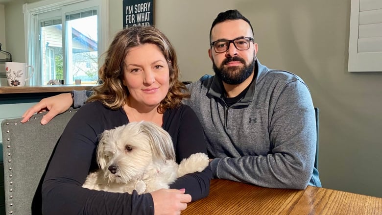 Matina and Karim Guirguis sit at their kitchen table. Matina is holding their dog. 