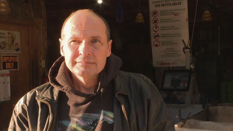 A man stands in front of a bottle depot on a sunny winter morning.