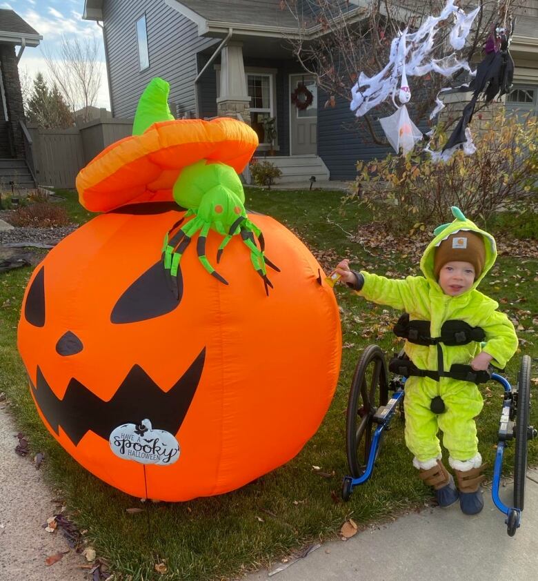 A small child is seen in a green costume and a walker beside a pumpkin. 