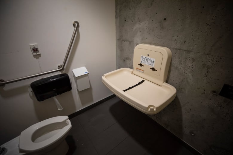 A baby change table is attached to a concrete wall in front of a toilet.