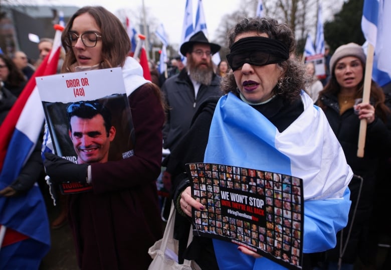 Two women, draped in flags, hold posters.