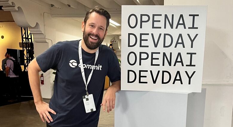 A man in a Commit t-shirt is pictured next to a sign that says OPENAI DEVDAY.