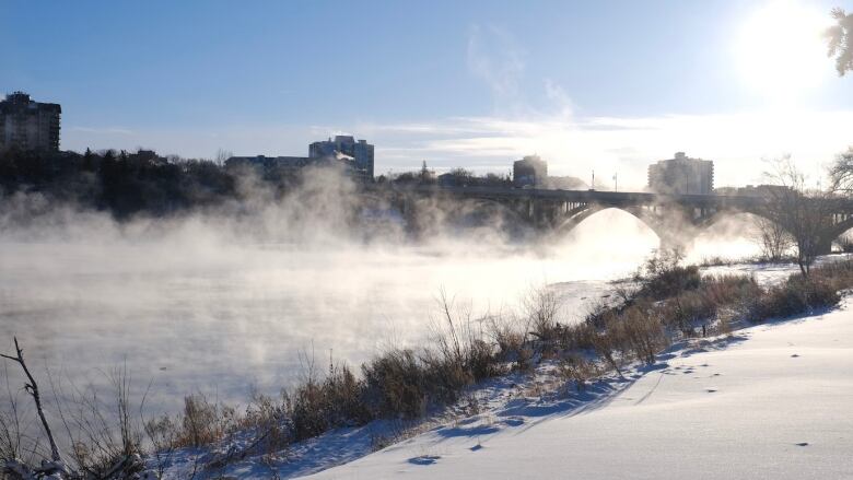 Mist rises over the South Saskatchewan River, with a bridge in the background.