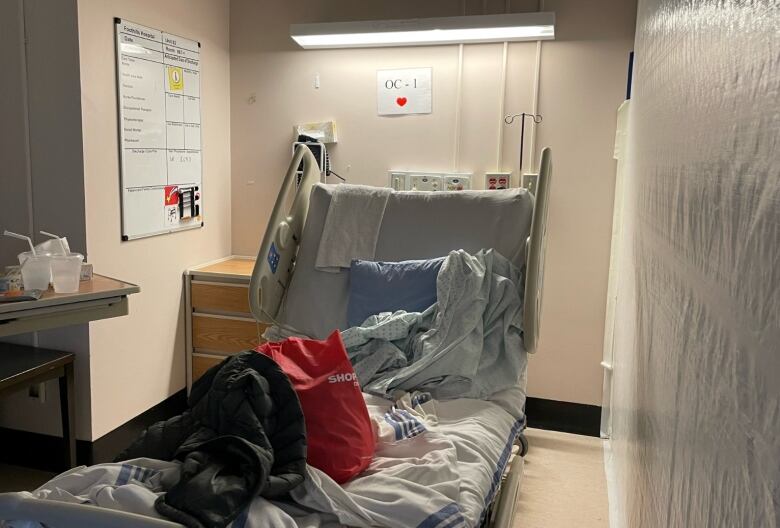 A hospital bed can be seen with white plastic sheeting hung from ceiling to floor, beside it