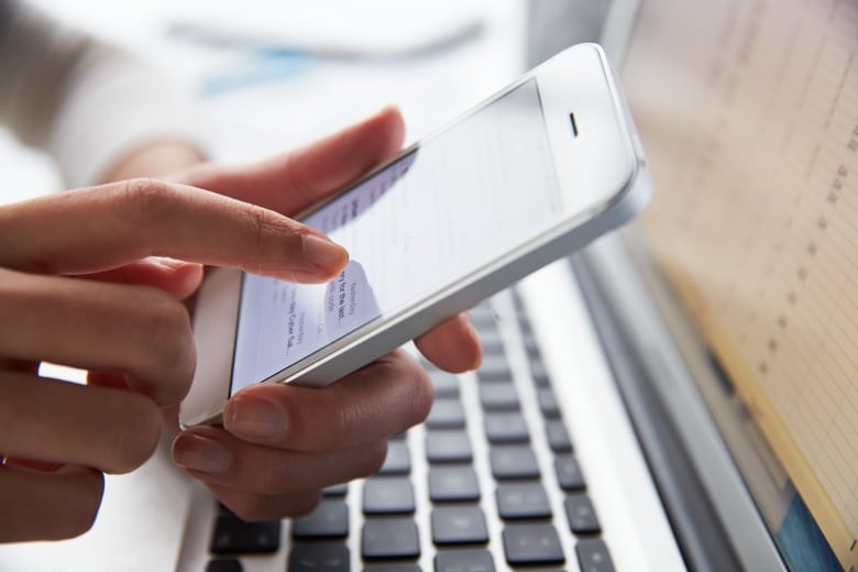 Close-up of a person's hand as they use a cellphone while over a laptop