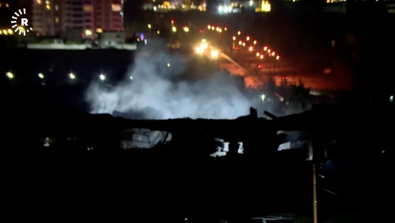 Smoke rises from a structure in the darkness in a nighttime photo.