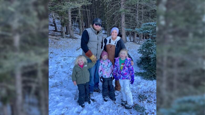 a man, a woman, three young children pictured standing in a snowy forest.