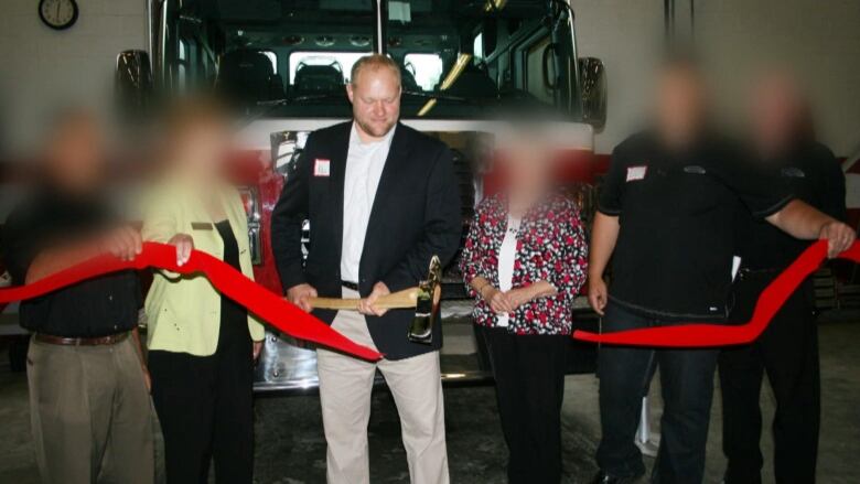 A business owner cuts a red ribbon with an axe. Other people around him are blurred out.