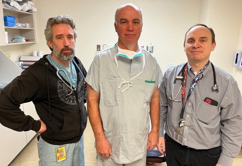 Three men, dressed in hospital scrubs, stand site by each.