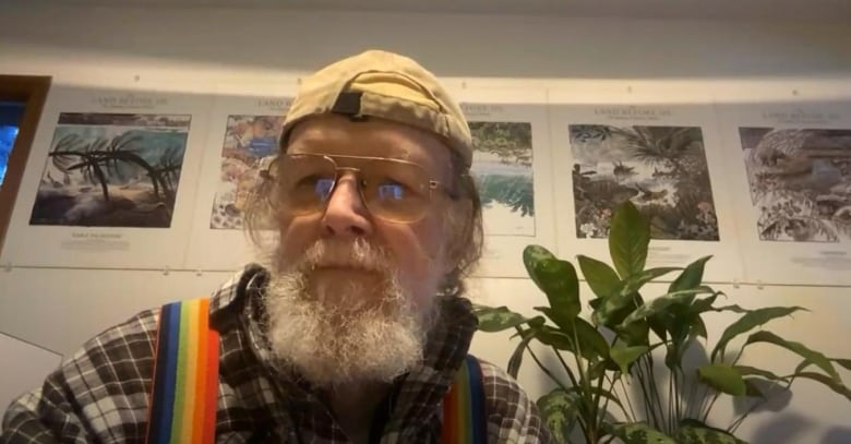 Man with white beard in flannel, hat, glasses and rainbow suspenders.