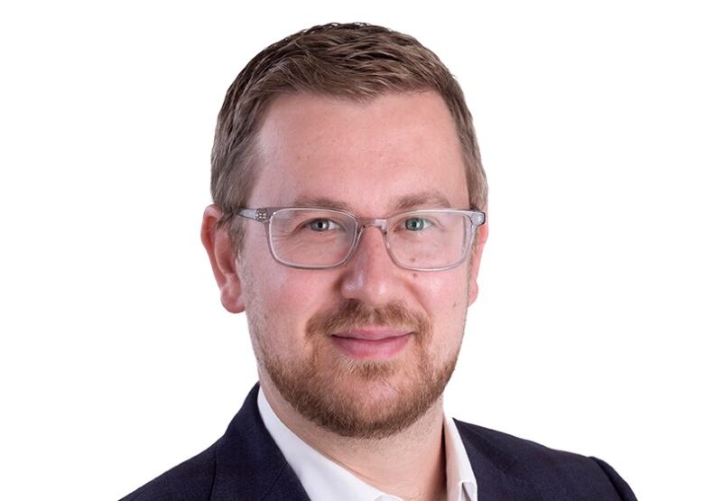 A man in glasses poses for a professional headshot.