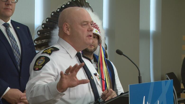 A bald-headed man in a police uniform speaks at a podium.