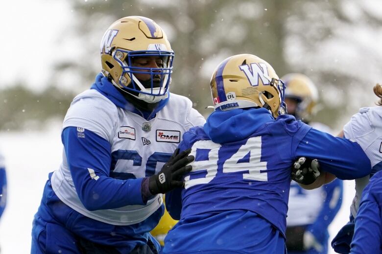 Two football players in white and blue jerseys collide during practice.