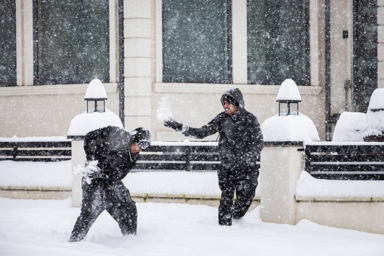 Two young men laugh as they throw snowballs at one another.