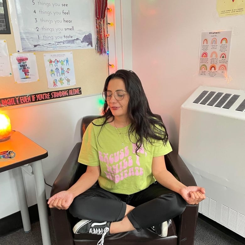 A woman sitting on a leather chair, with her legs crossed, her arms on her knees and her hands turned upwards. She looks calm and collected, sitting in the lotus position.