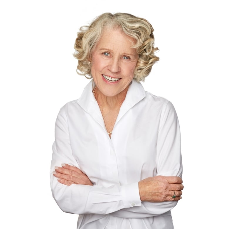 A woman in a white blouse smiles at the camera. Her arms are crossed. 