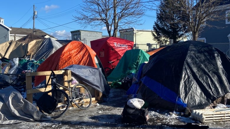 A group of tightly spaced and colourful tents and tarp enclosures with apartment buildings in the background. 