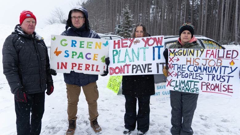 Four people in winter jackets hold colourful protest signs in the snow