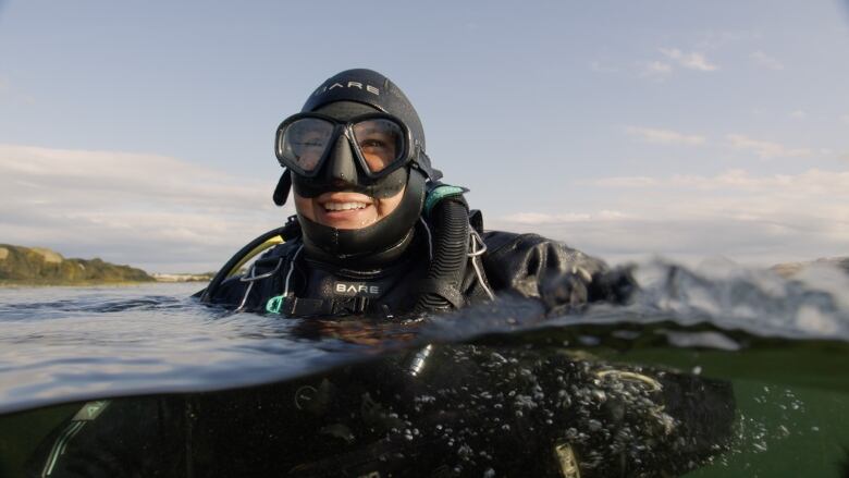 A woman wearing scuba gear floats at the surface with a big smile on her face. 