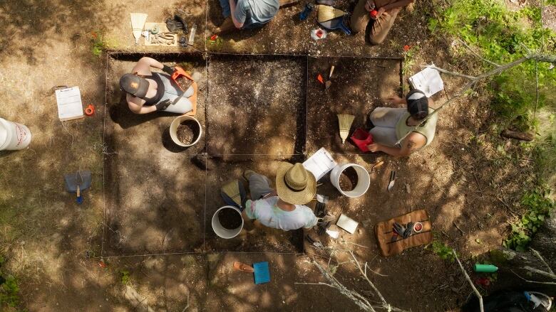 An overhead shot of three archaeologists digging in square plots of dirt. 