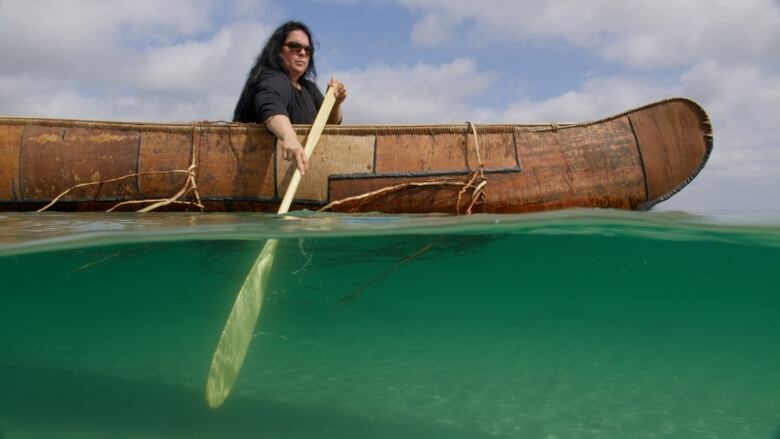 An Indigenous woman paddles a birchbark canoe. 