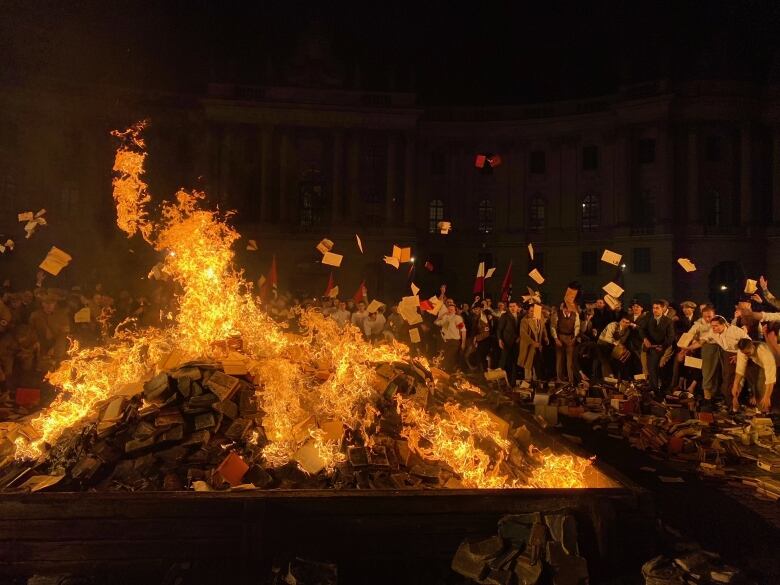 People throw books on a raging fire at night