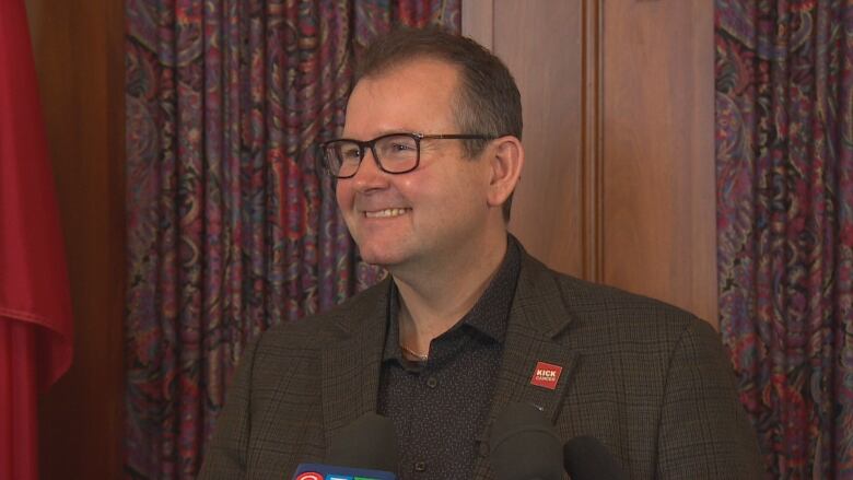 A man wearing a blazer smiles while standing behind a podium. 