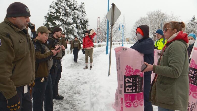 A row of park rangers stand opposite people carrying insulation amid heavy snow.