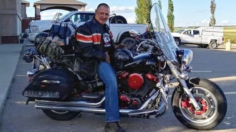 A man wearing a leather jacket sits on a motorcycyle.