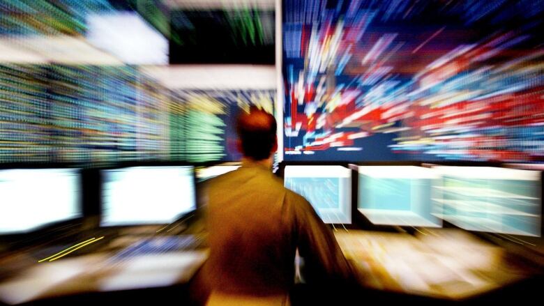 A man stands in front of a bank of computer monitors.