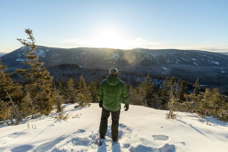 Man stands at the top of a mountain in winter overlooking scenery below.