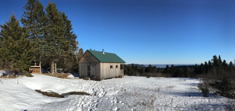 A winter hilltop scene showing lots of snow and a small rustic cabin.