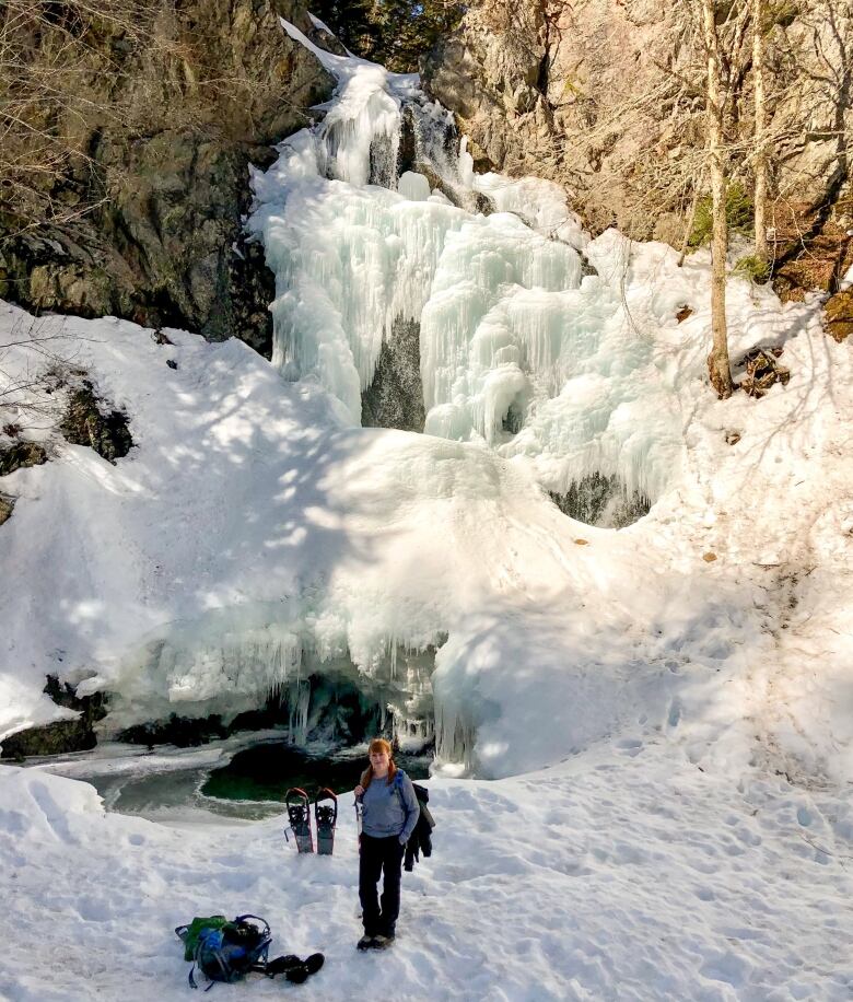 Hiker stands in front of massive frozen waterfall.