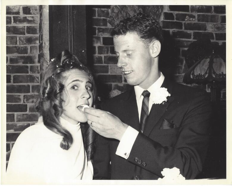 A black and white photo of a groom feeding a bride a piece of cake.