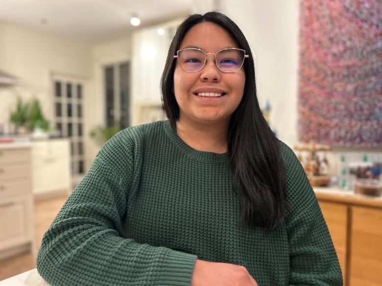 young woman wearing clear glasses and a green sweater smiling at the camera