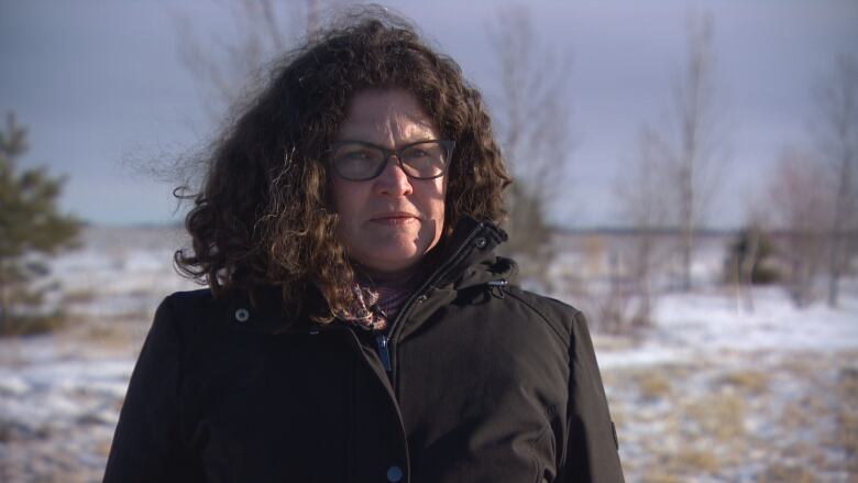 A woman stands in front of a row of trees planted next to the Trans-Canada Highway.