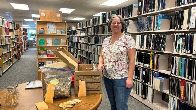 A woman stands in a library beside an open box that's sitting on a table.